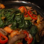 Meat, vegetables, spinach stirred in cast iron skillet.